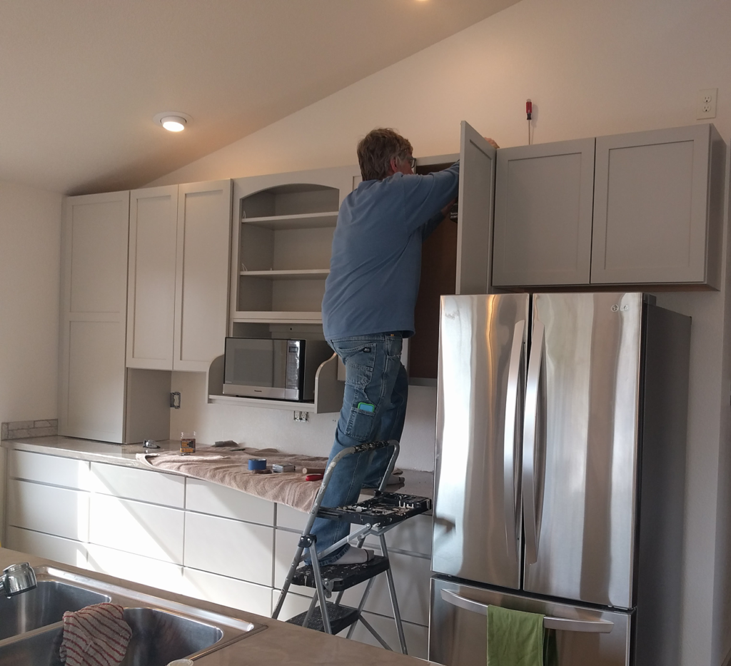 Husband installing cabinets after building our house.  Note shiny refrigerator .
